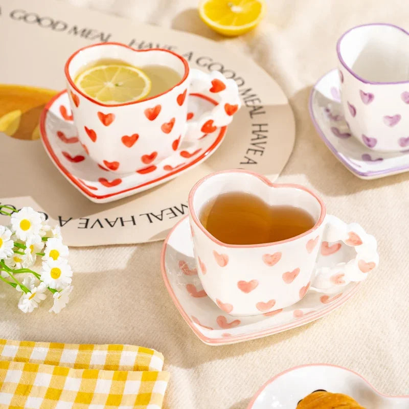 Heart-shaped tea cups with lemon slices on a table with a checkered cloth and flowers.