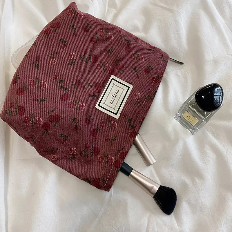 Floral-patterned makeup bag with a brush and perfume bottle on a white surface