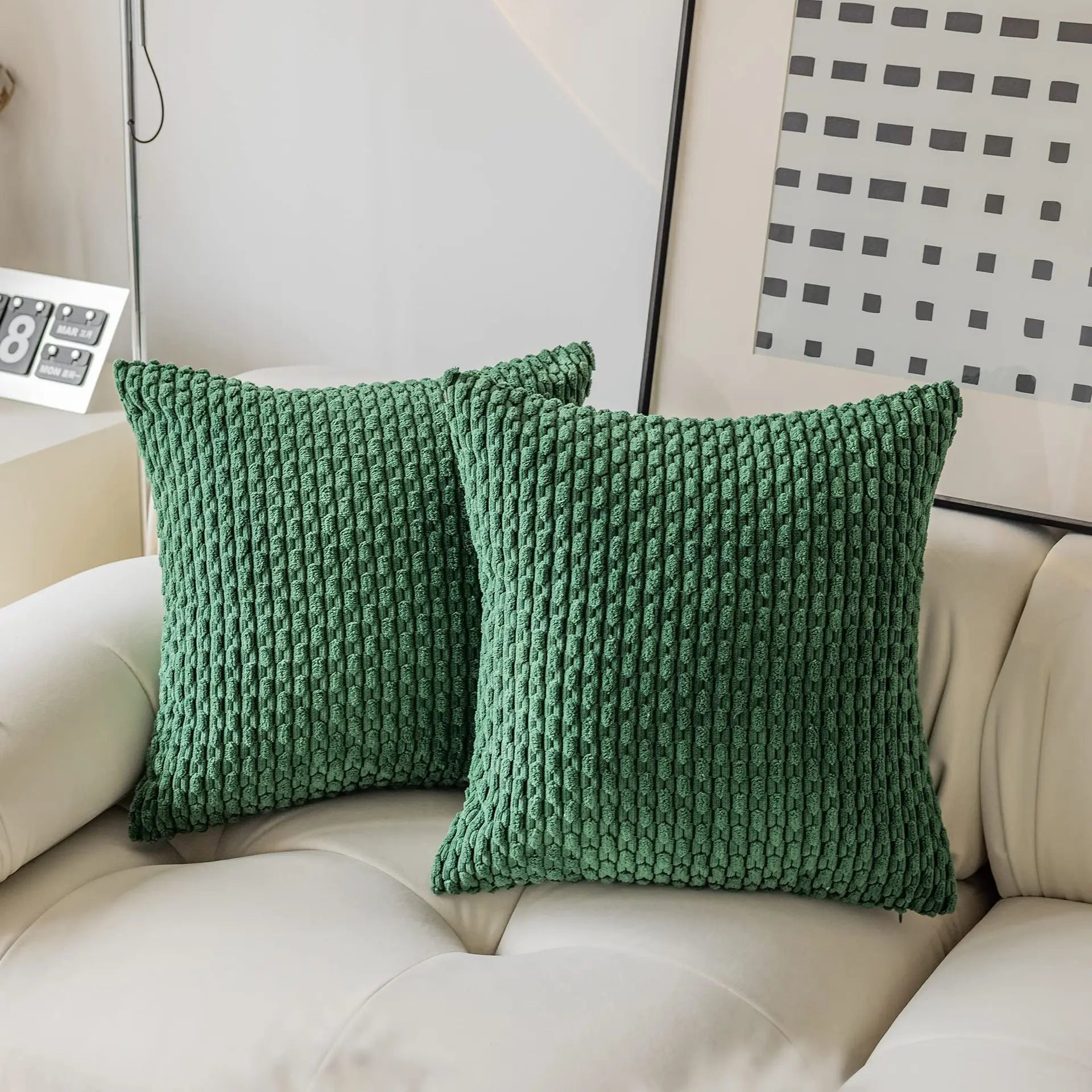 Two green textured pillows on a beige sofa with a decorative wall in the background.
