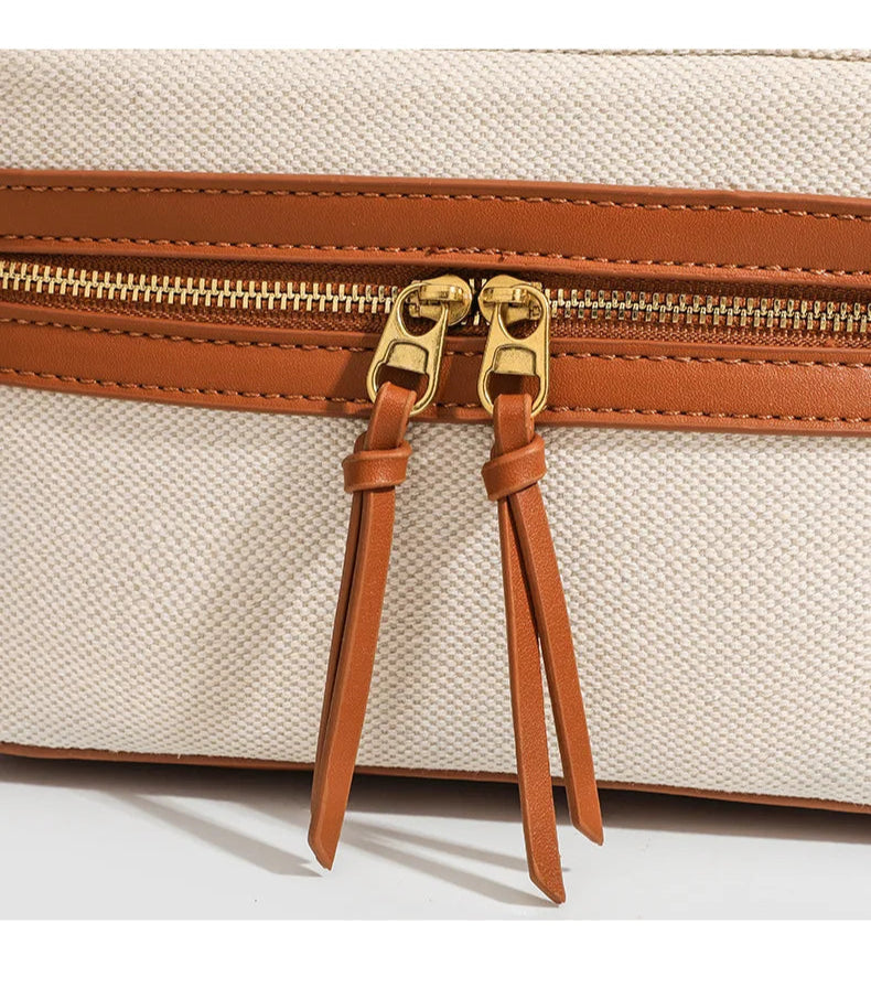 Beige handbag with brown leather straps and zipper on a white background