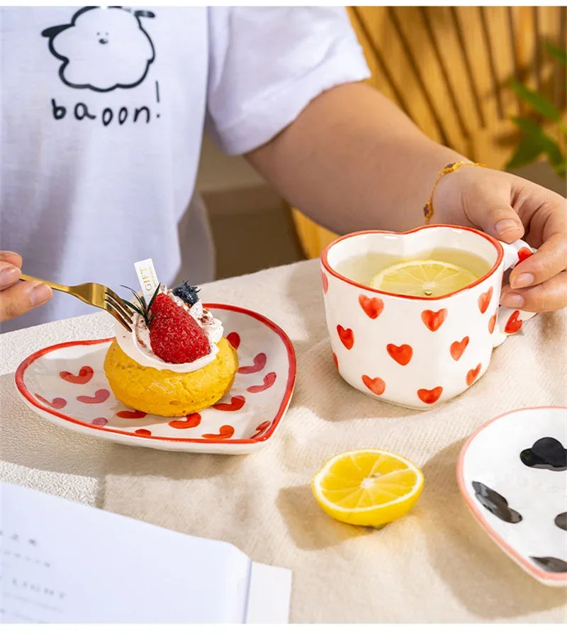 Person holding a heart-patterned mug with a dessert and lemon on a table.