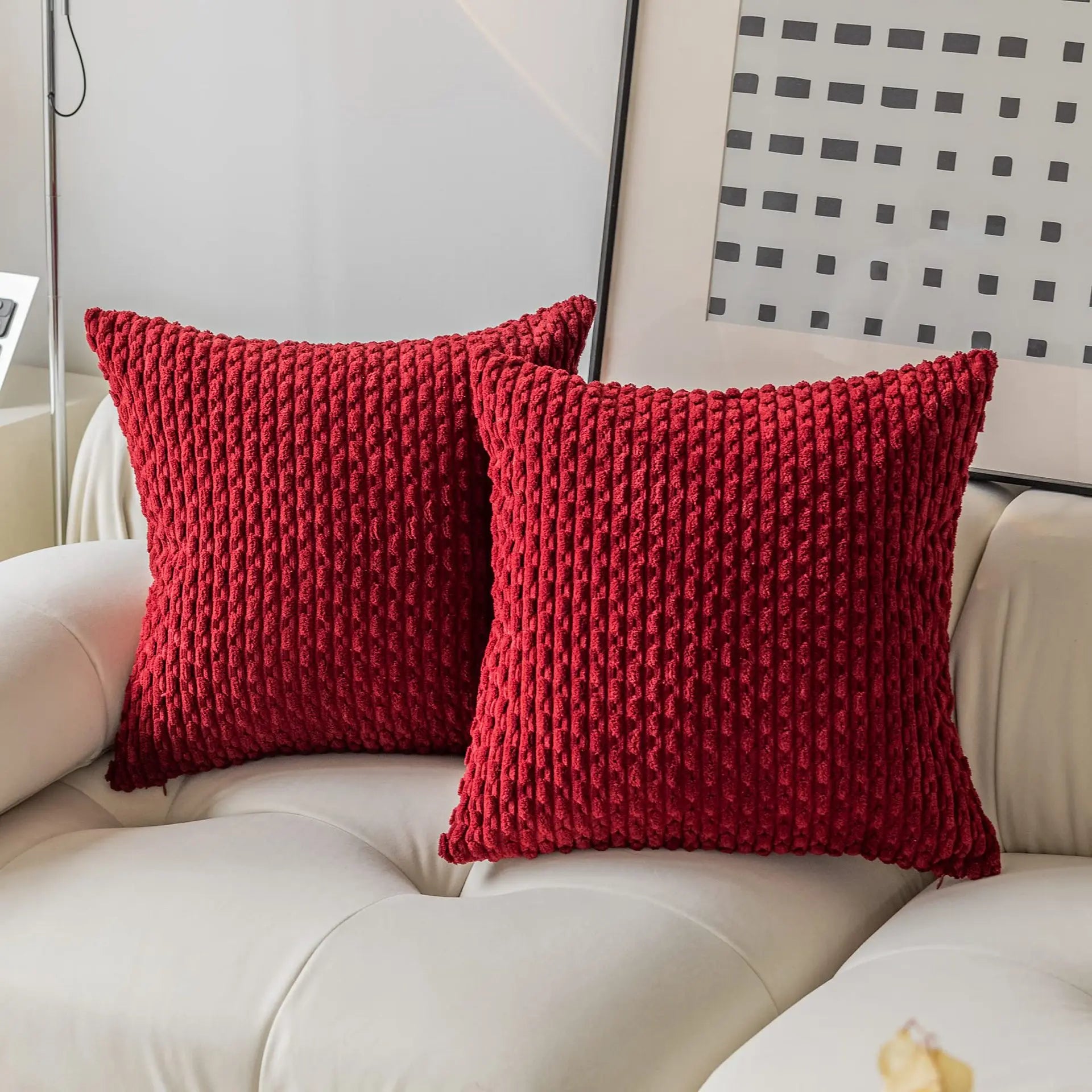 Two red textured pillows on a beige sofa with a decorative wall in the background.