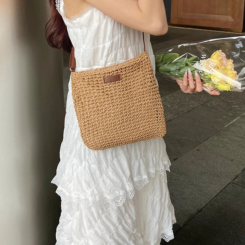 Woman holding a woven bag and a plastic bag with flowers on a sidewalk.