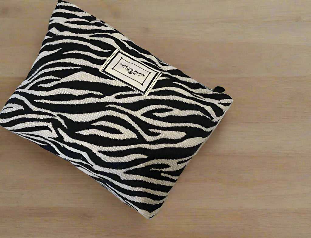Zebra-patterned pouch on a white surface with a candle and small container.