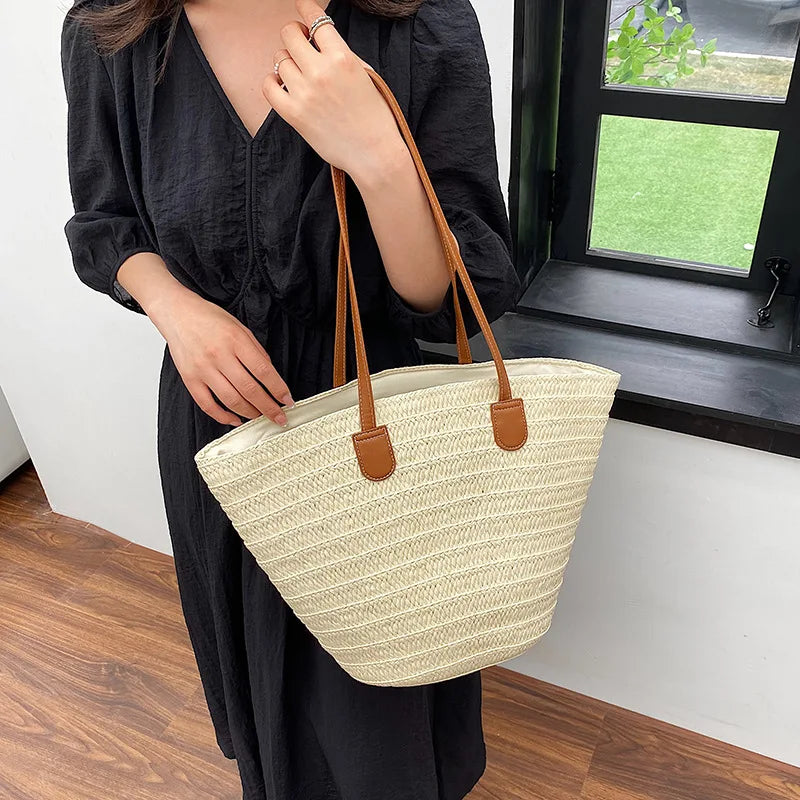 Person holding a beige woven bag with brown straps indoors.