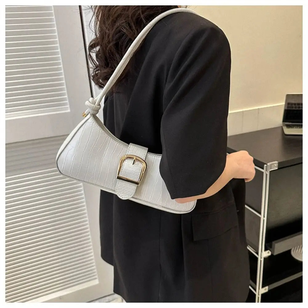 Person wearing a white handbag with a gold buckle in an indoor setting