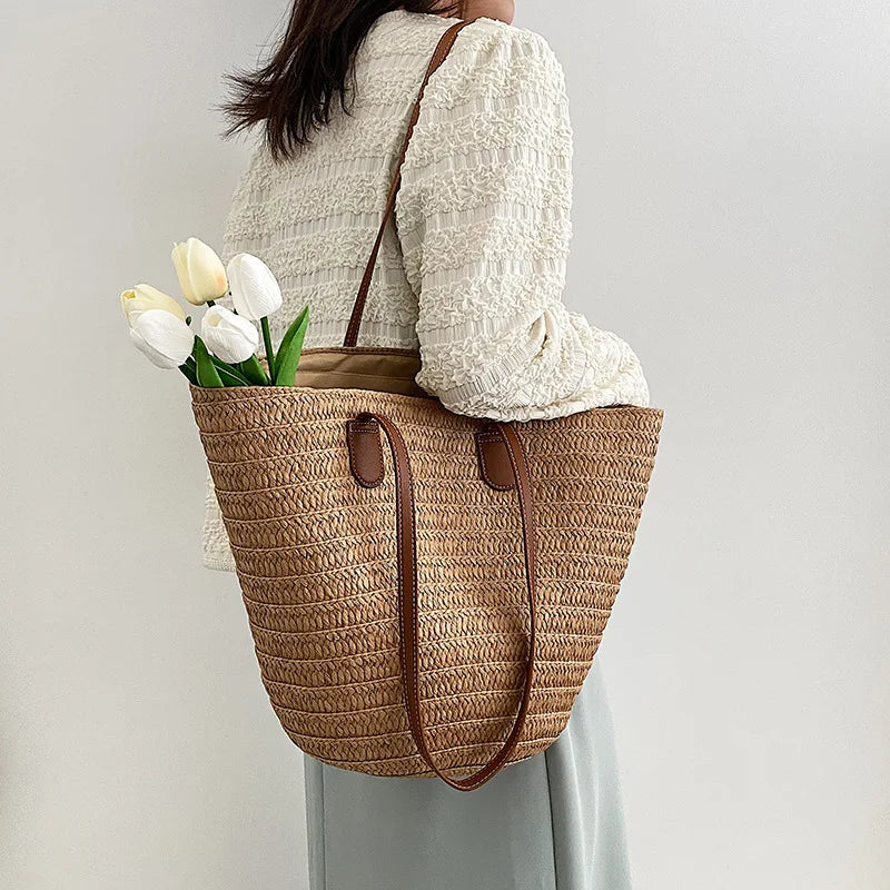 Person holding a straw tote bag with flowers against a plain background