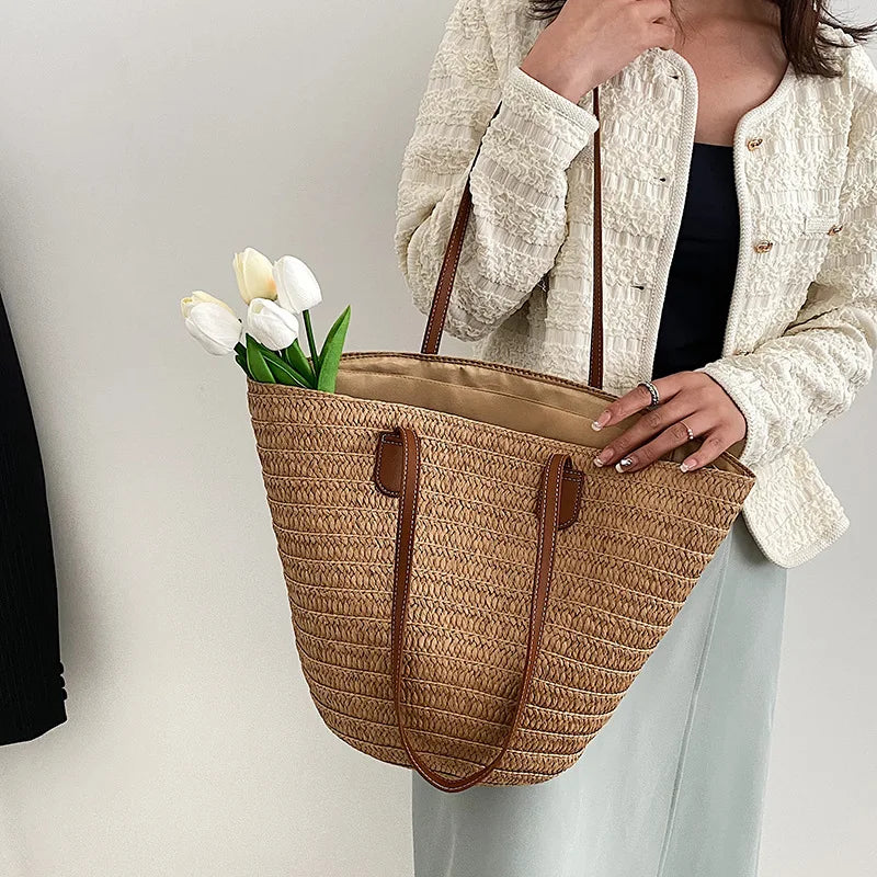 Person holding a straw tote bag with flowers against a neutral background