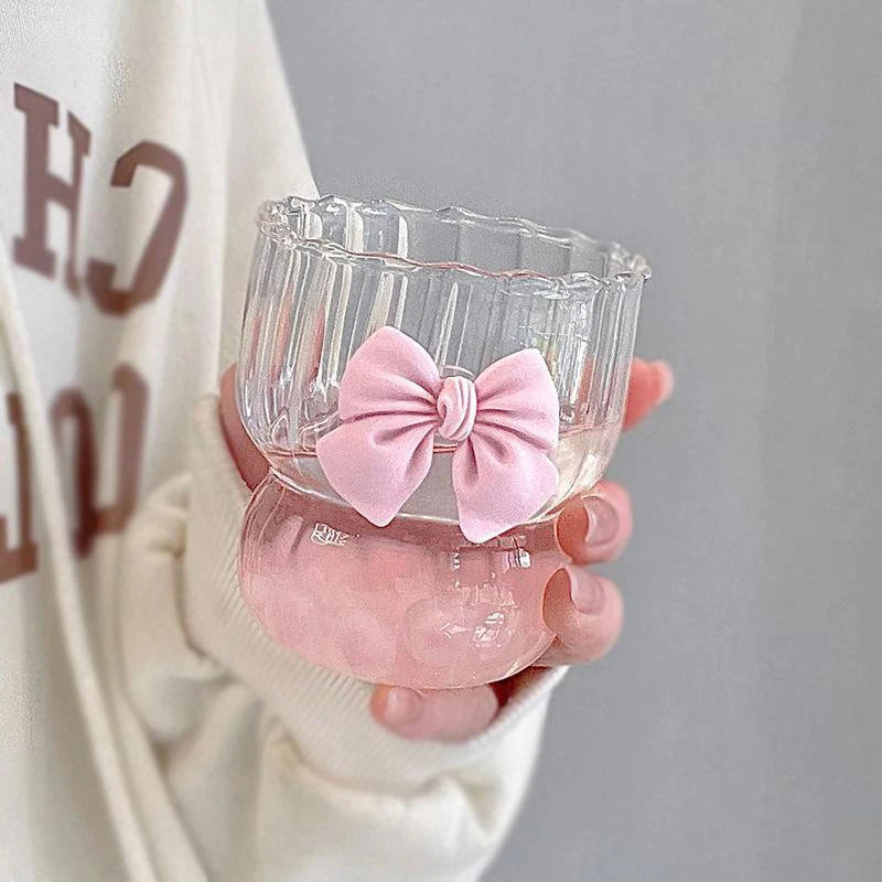 Clear glass container with a pink bow held by a person wearing a white sweater with red text.