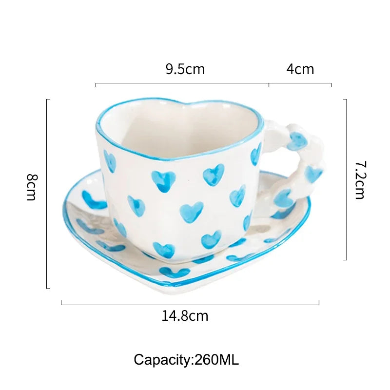 Heart-shaped ceramic cup with blue heart patterns and saucer, shown with measurements on a white background.