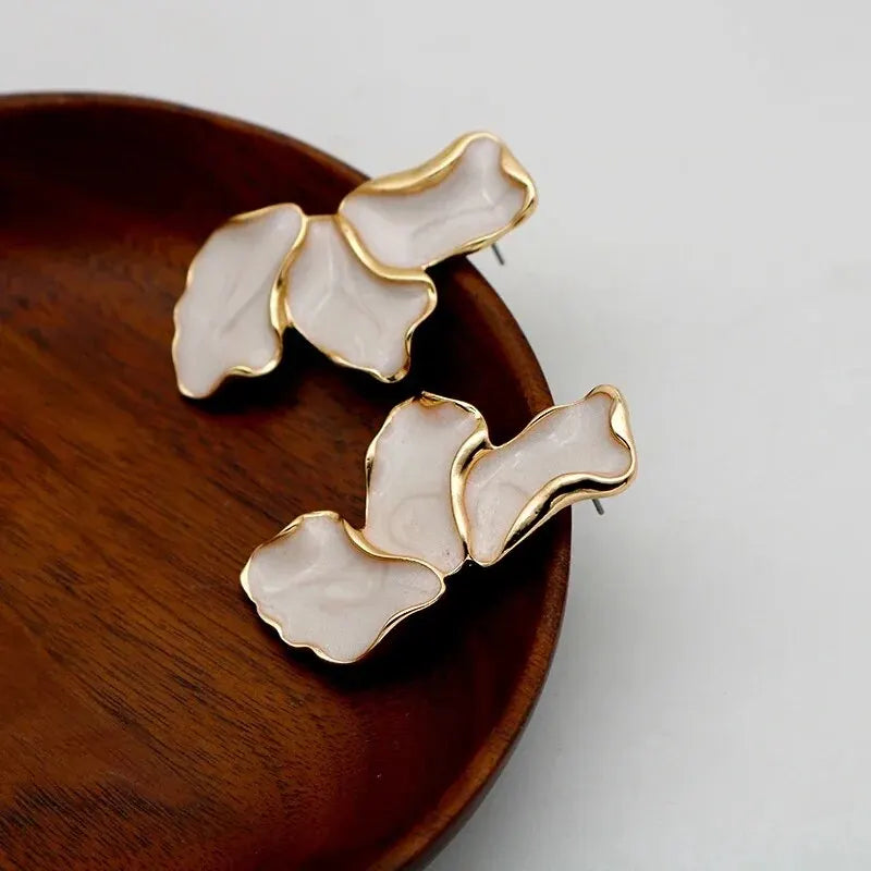 Pair of gold and white floral earrings on a wooden surface.