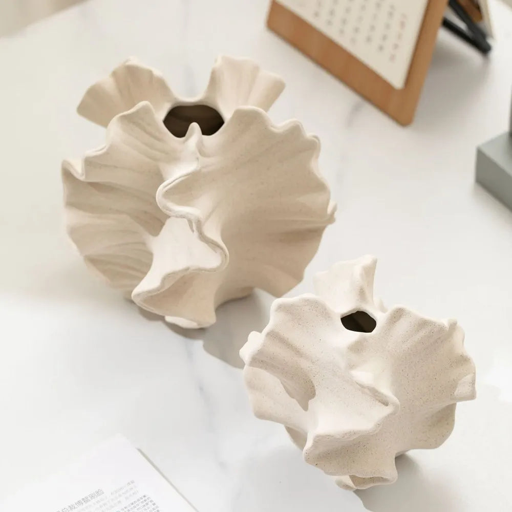 Two beige ceramic shell-shaped vases on a light surface.