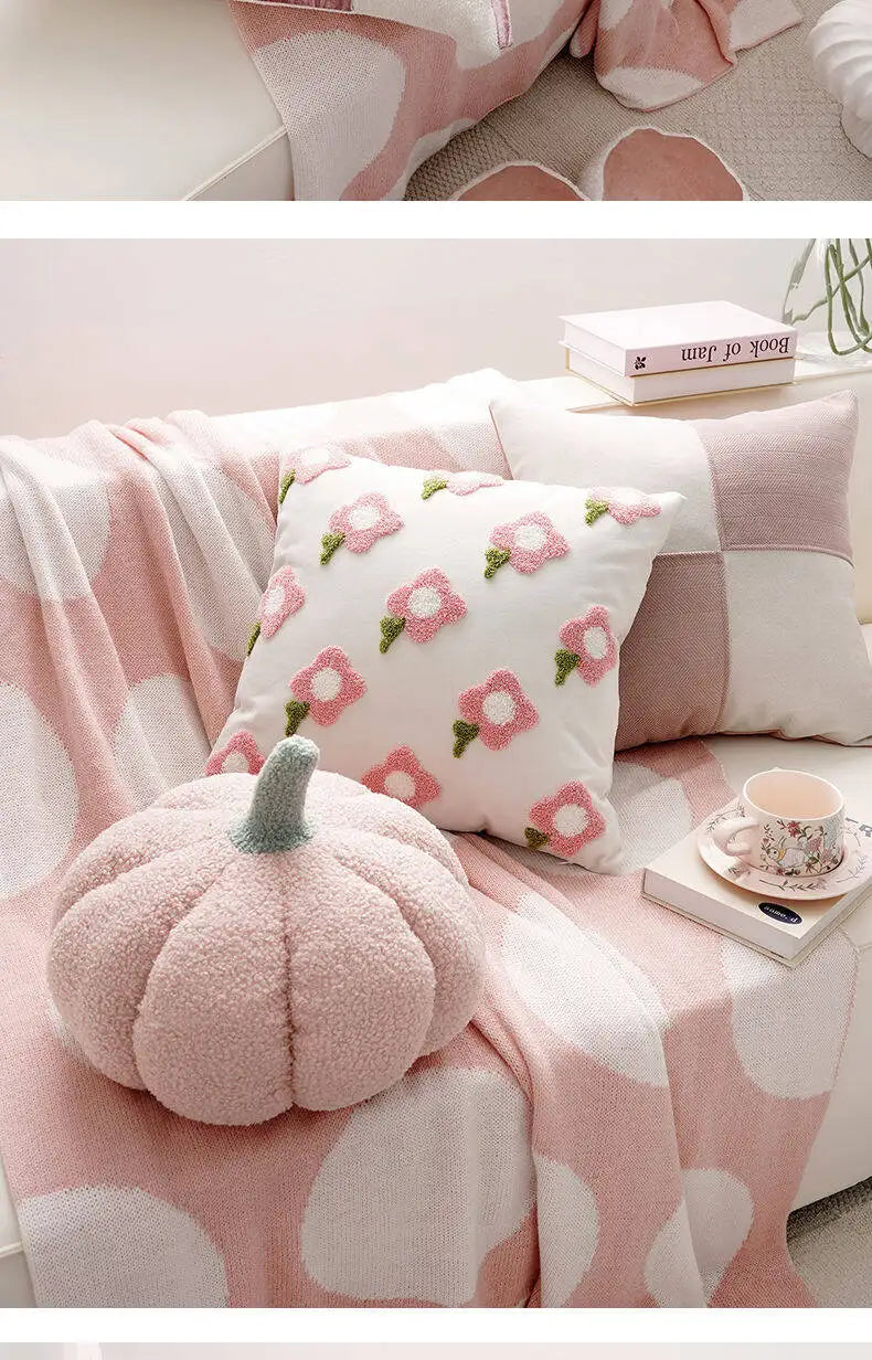 Pink floral pillow and pumpkin-shaped cushion on a pink blanket with a book and teacup in the background.