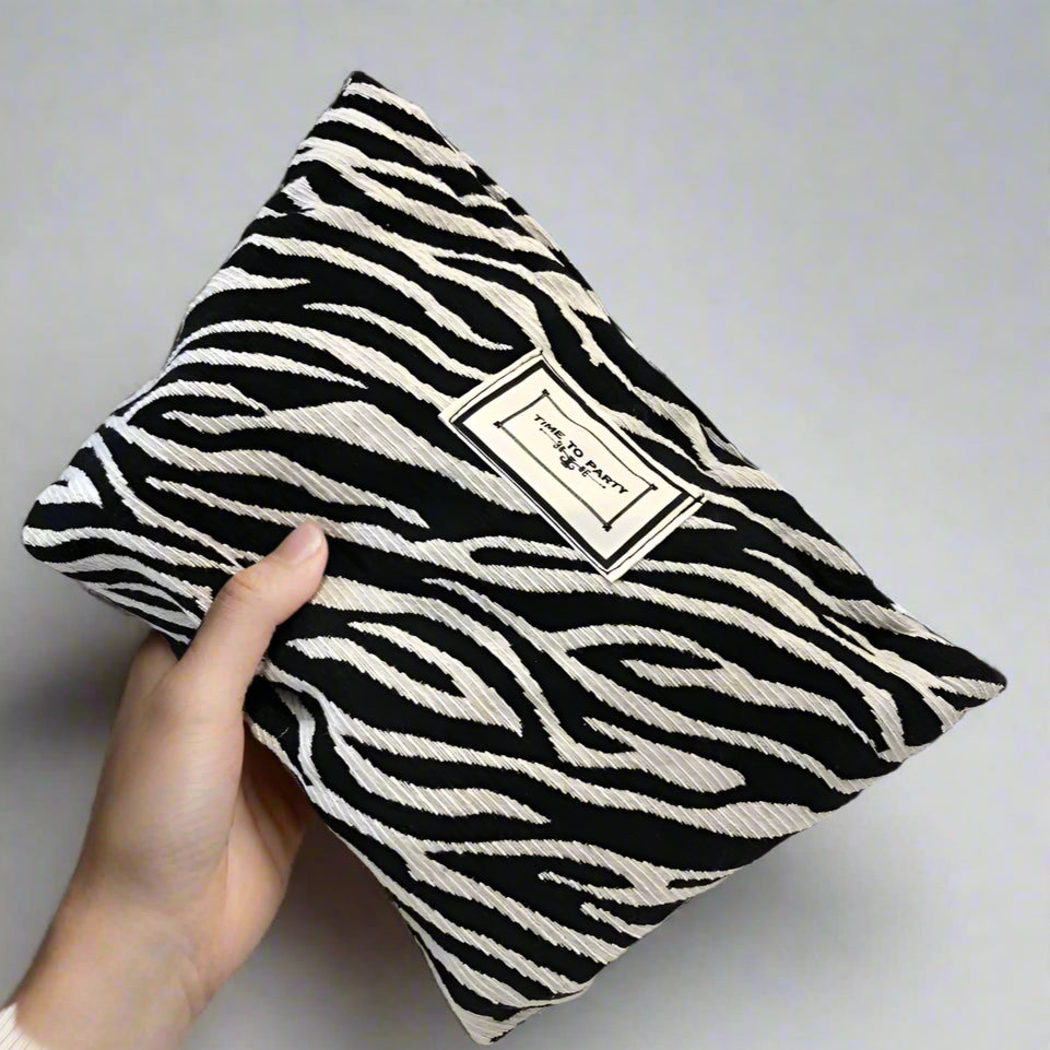 Black and white zebra-striped pillow held by a hand with a label on a blurred indoor background