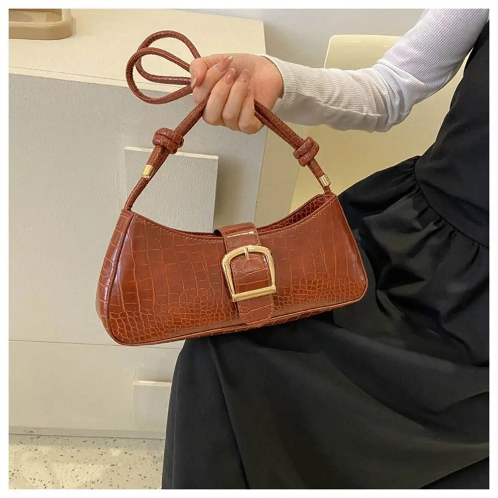 Brown handbag with gold buckle held by a person in a kitchen setting