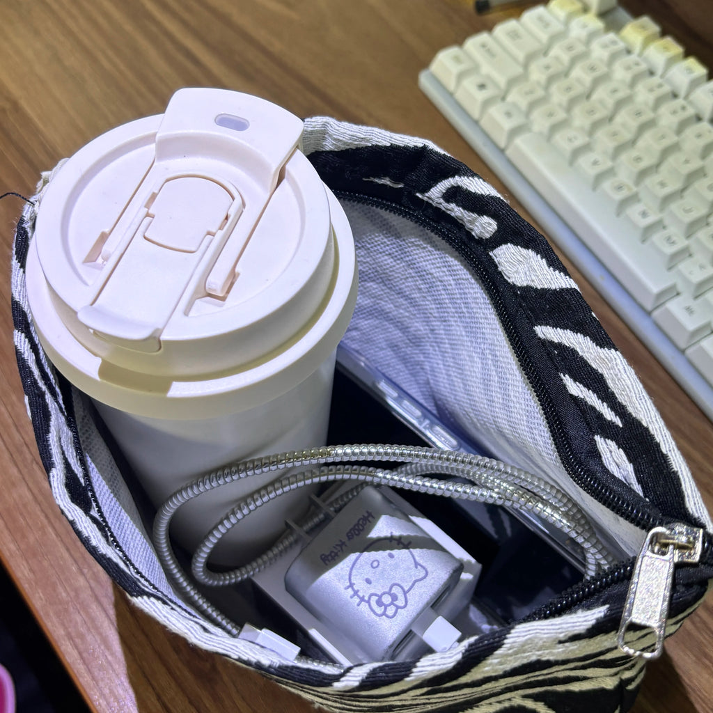 White travel mug with a zebra-patterned bag and keyboard in the background