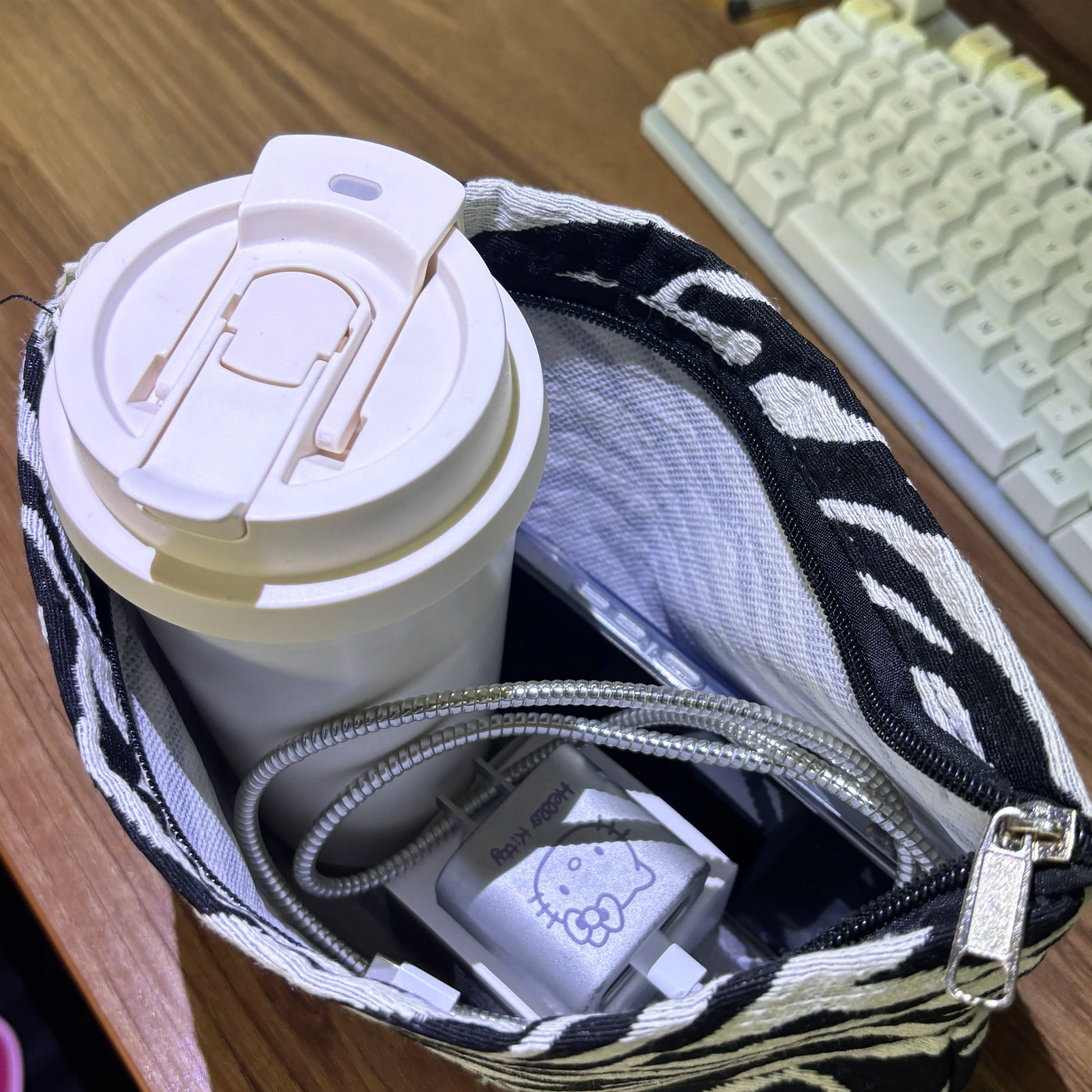 White travel mug with a zebra-patterned bag and keyboard in the background