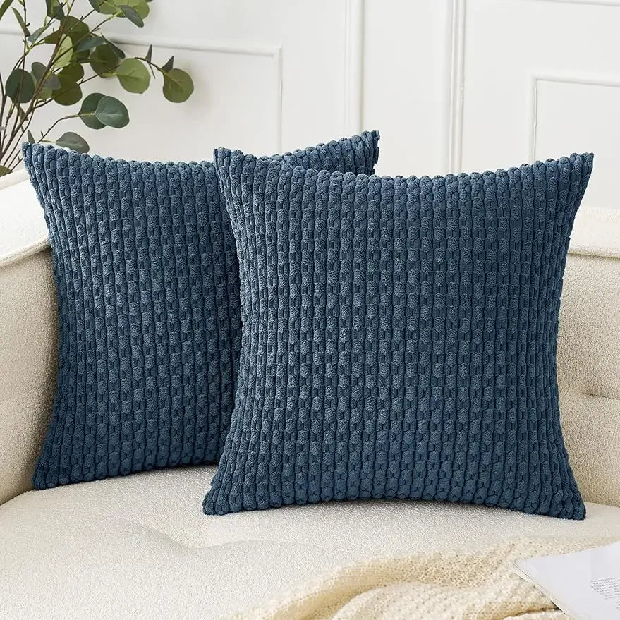 Two blue textured pillows on a beige couch with a white wall and plant in the background.
