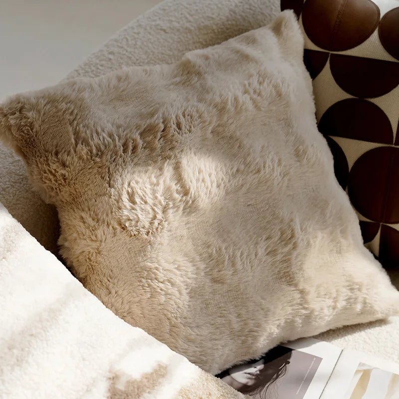 Close-up of fluffy beige pillows on a couch with a patterned wall in the background.