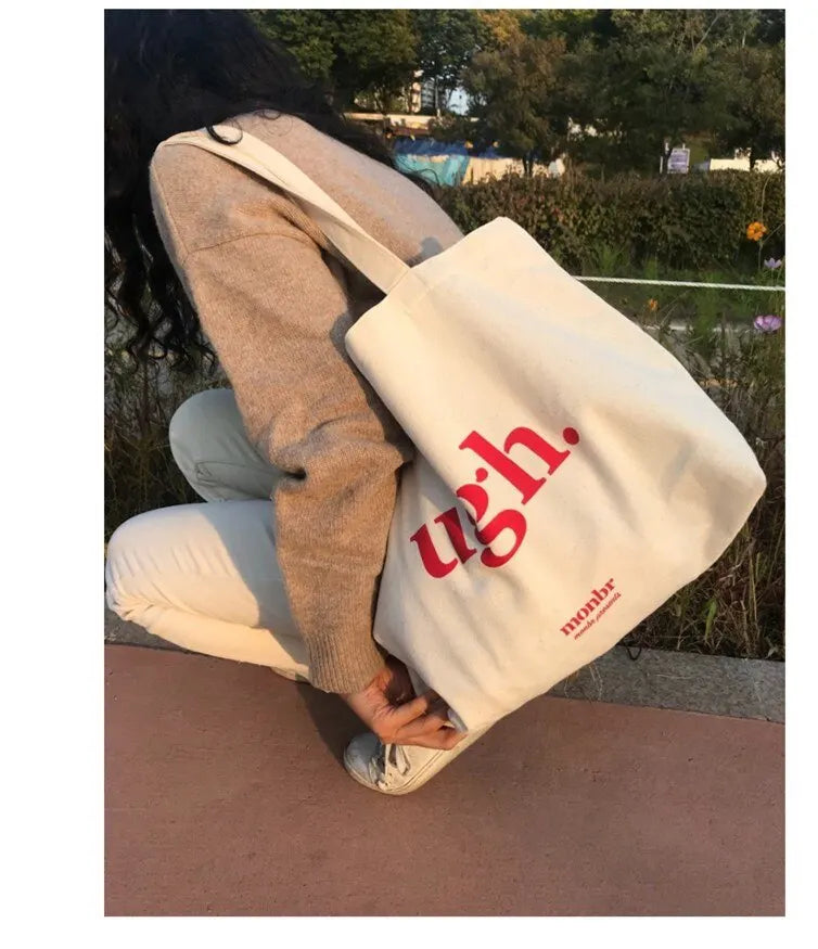 Person holding a white tote bag with red text outdoors