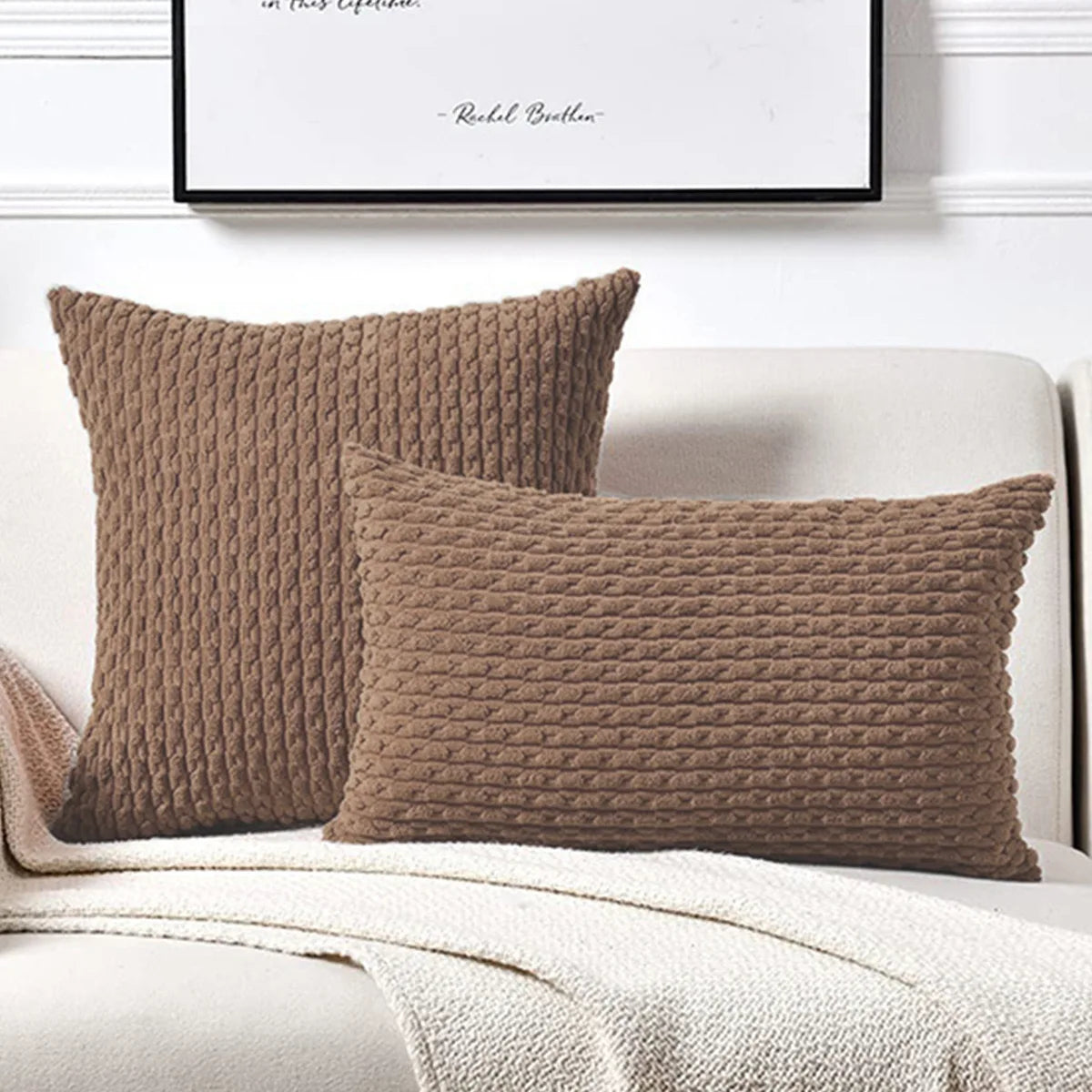Two brown textured pillows on a white sofa with a framed picture in the background.