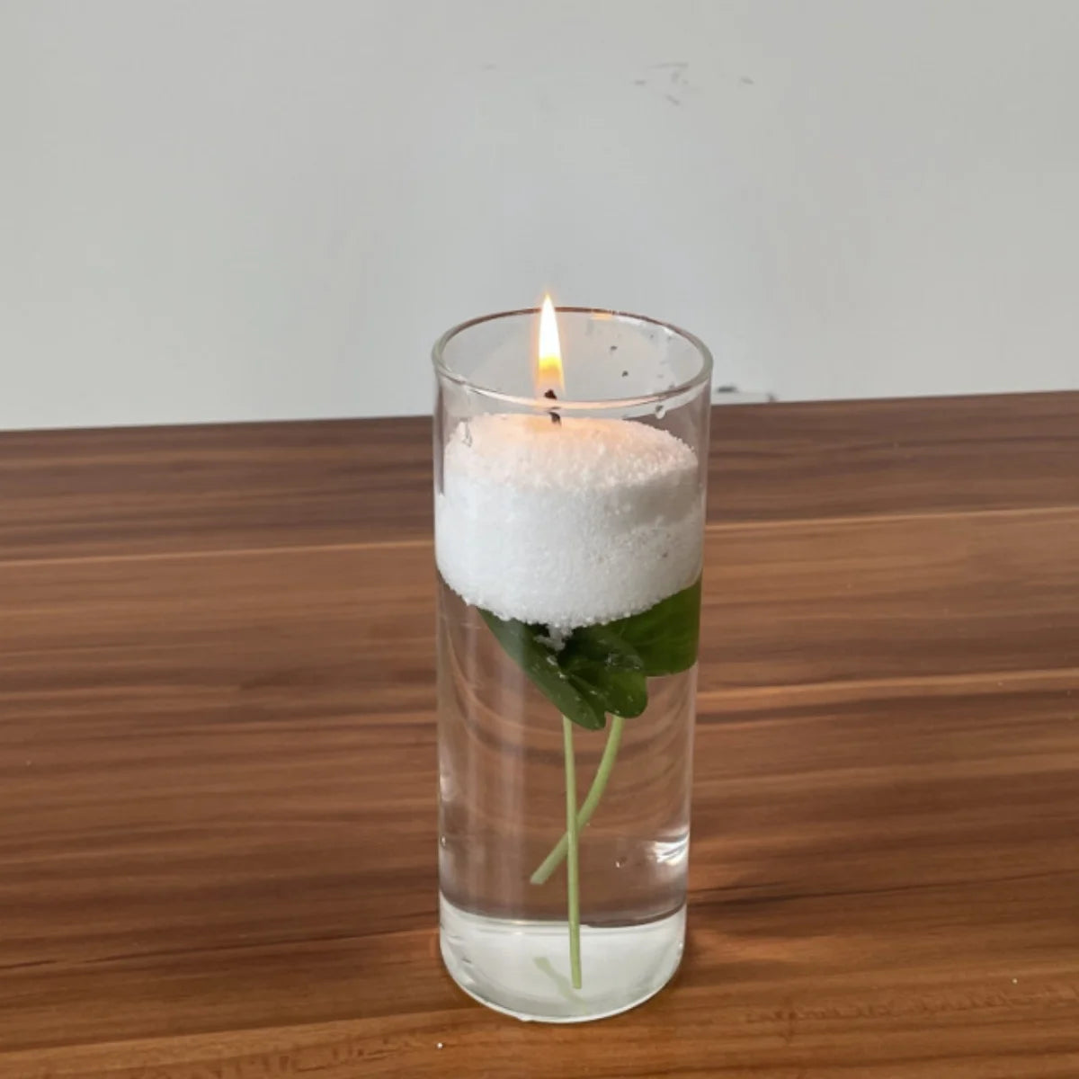 Candle in a glass with water and a leaf on a wooden surface