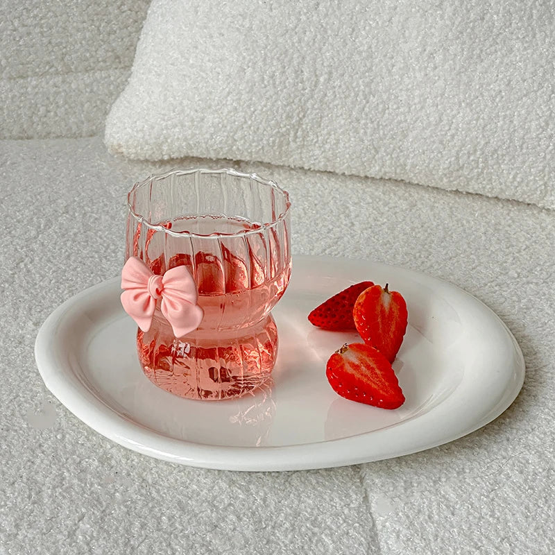 Pink glass with a bow and strawberries on a white plate against a light gray background