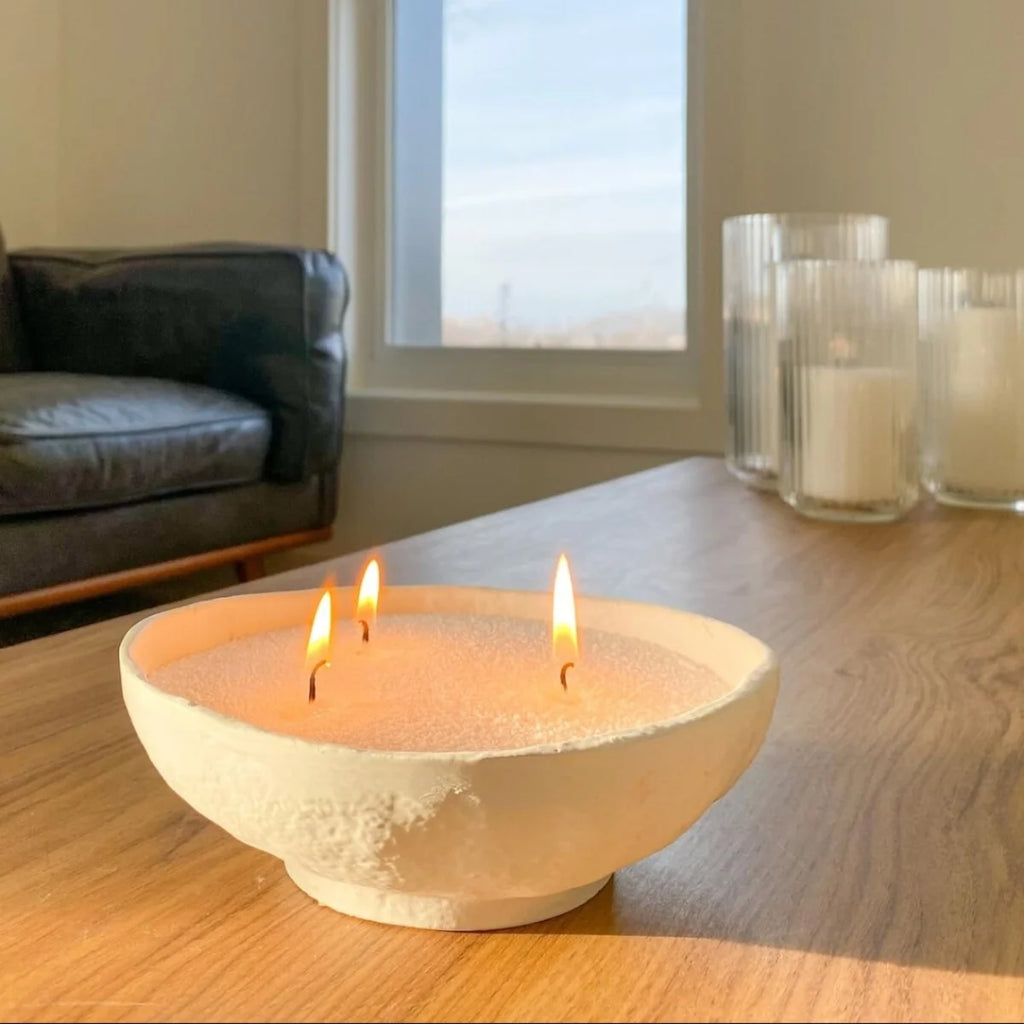 Ceramic bowl with three lit candles on a wooden table in a living room.