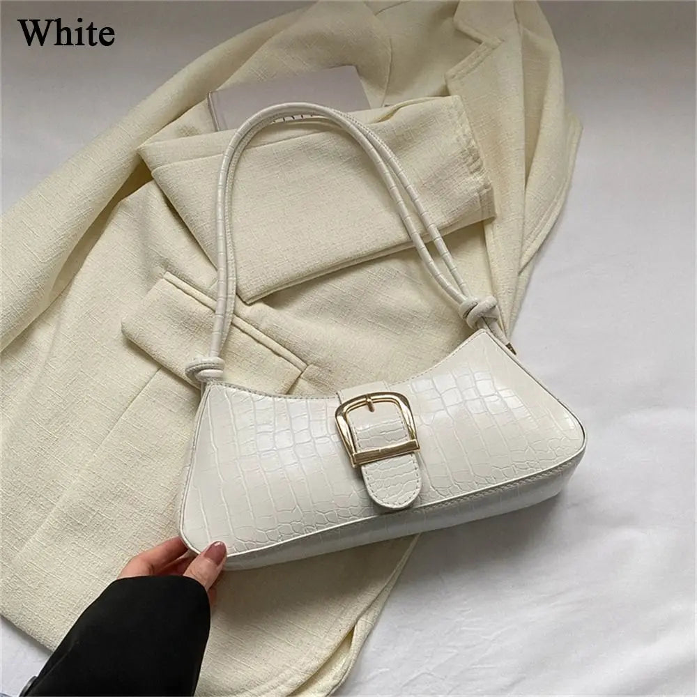 White handbag with gold buckle held by a hand on a white surface with a beige coat.