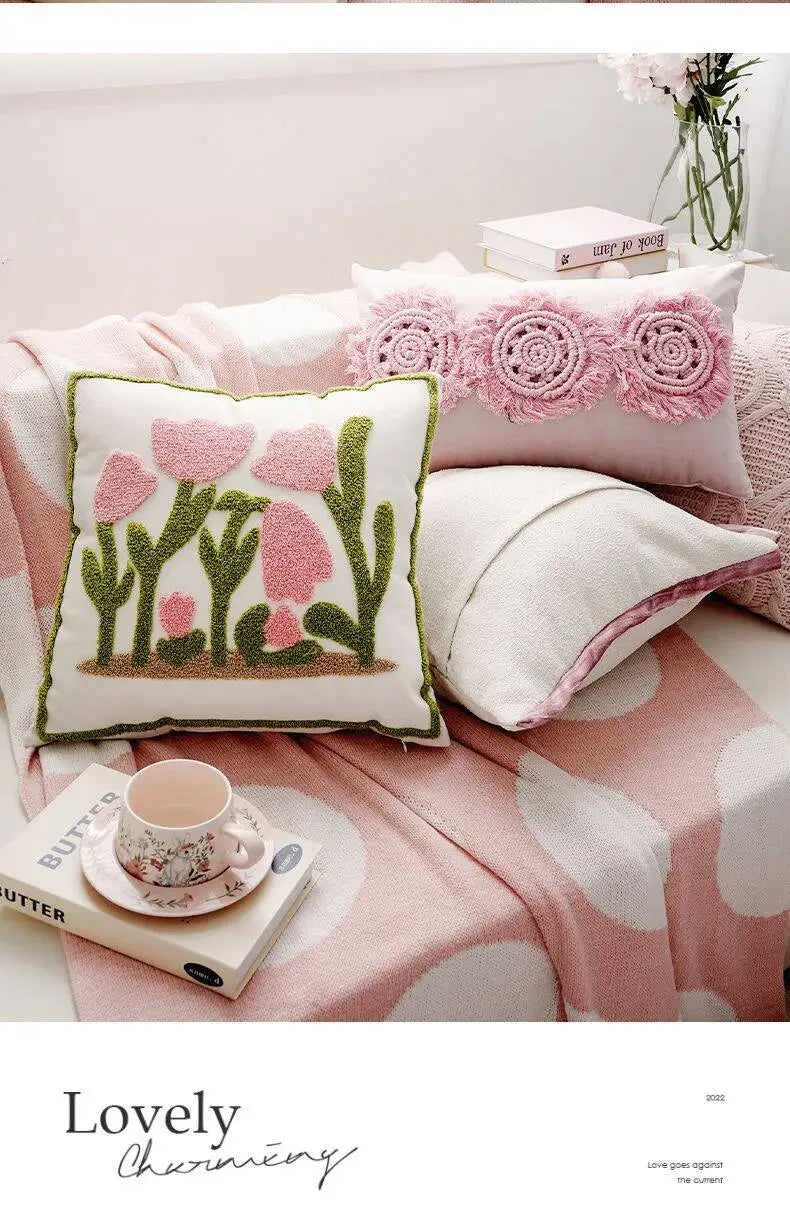 Decorative pillows with floral patterns on a bed with a pink blanket.