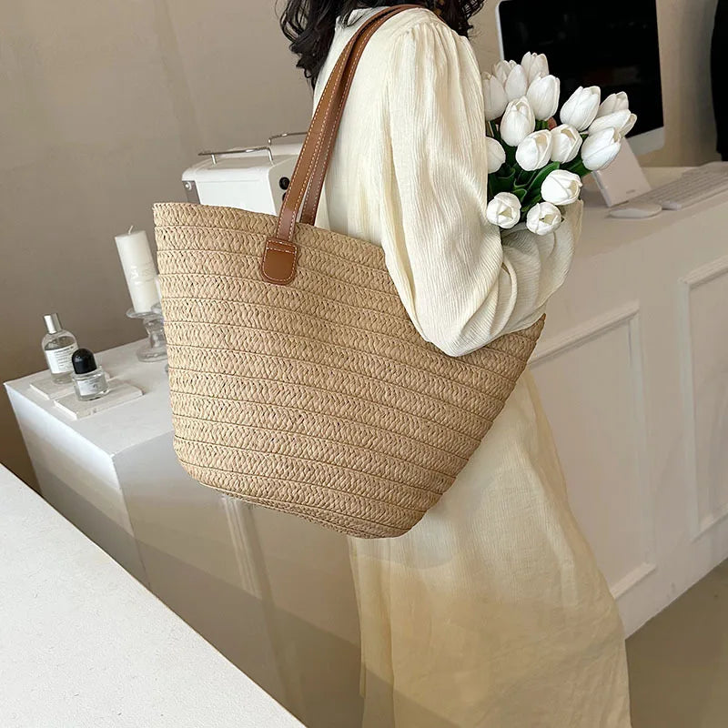 Person holding a straw bag with a bouquet of white tulips indoors.
