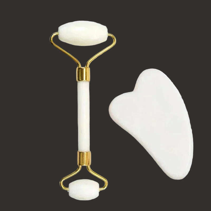 White and gold facial roller and gua sha tool on a dark background
