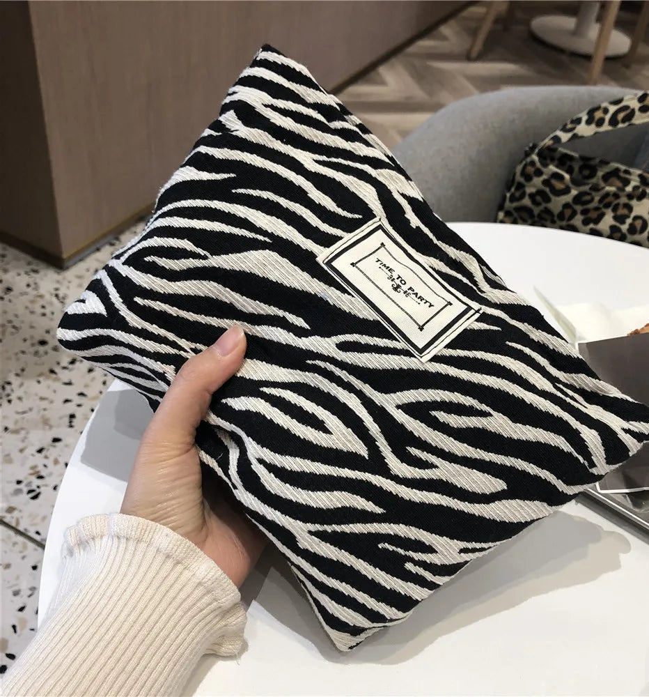 Black and white zebra-striped pillow held by a hand with a blurred indoor background
