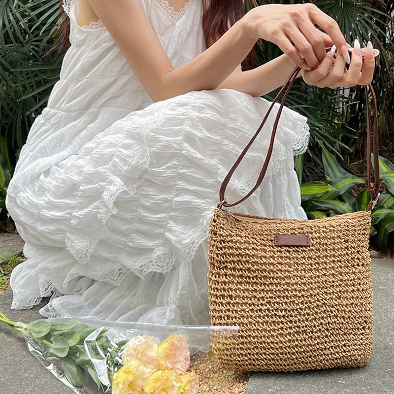 Woman in a white dress holding a woven bag with flowers on the ground.