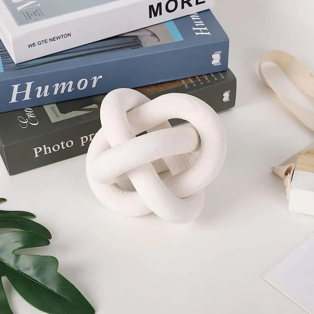 White knot sculpture on a surface with books and a plant leaf in the background