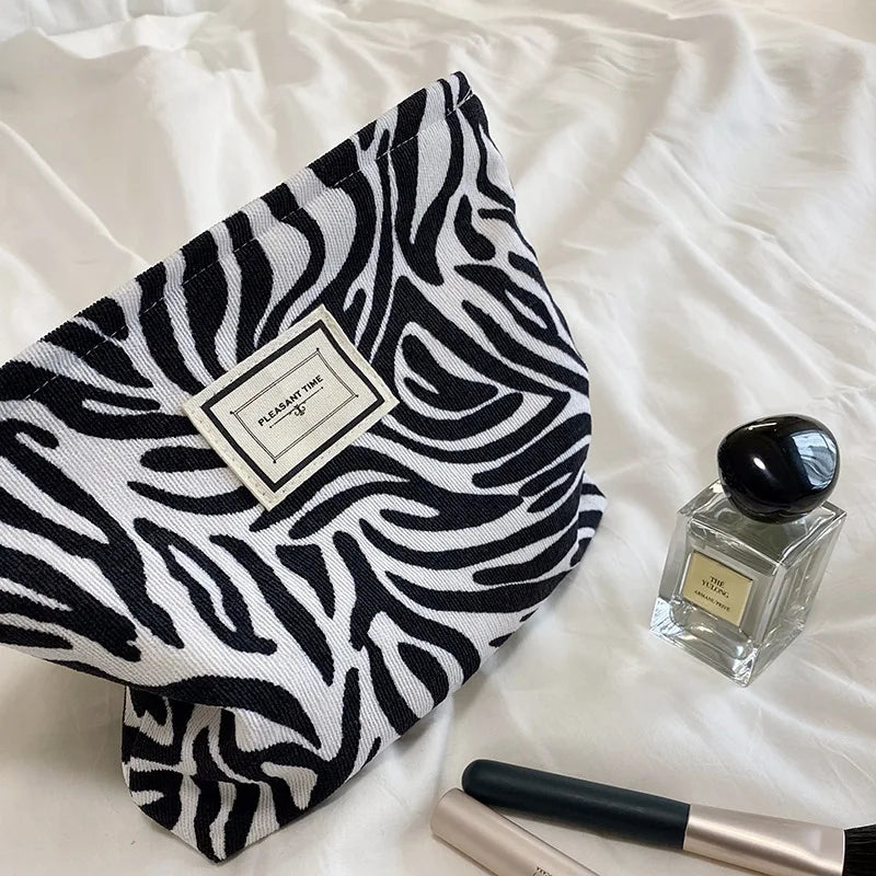 Zebra patterned pouch with a perfume bottle and makeup brush on a white surface