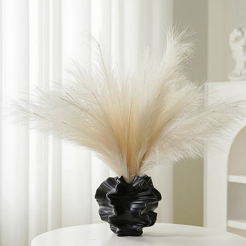 Black coral vase with dried pampas grass against a white curtain background