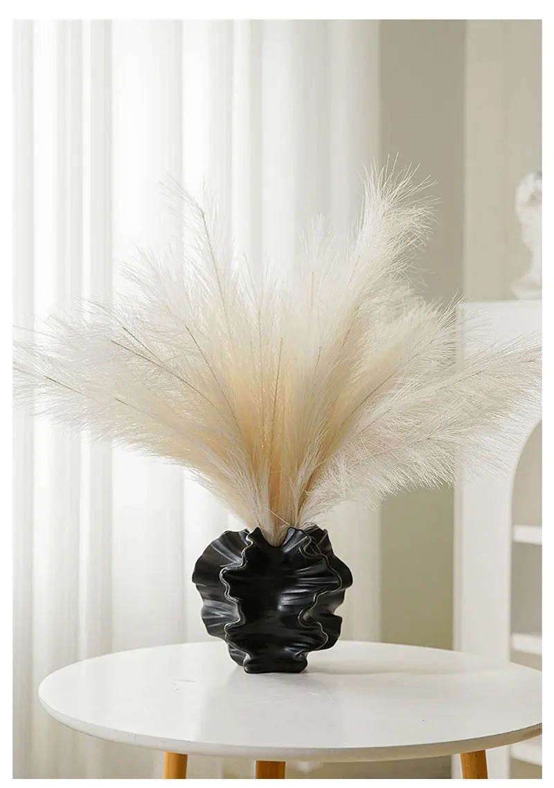 Black vase with dried pampas grass on a white table against a neutral background