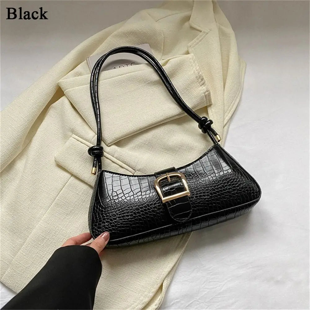 Black crocodile-patterned handbag held by a hand against a light background