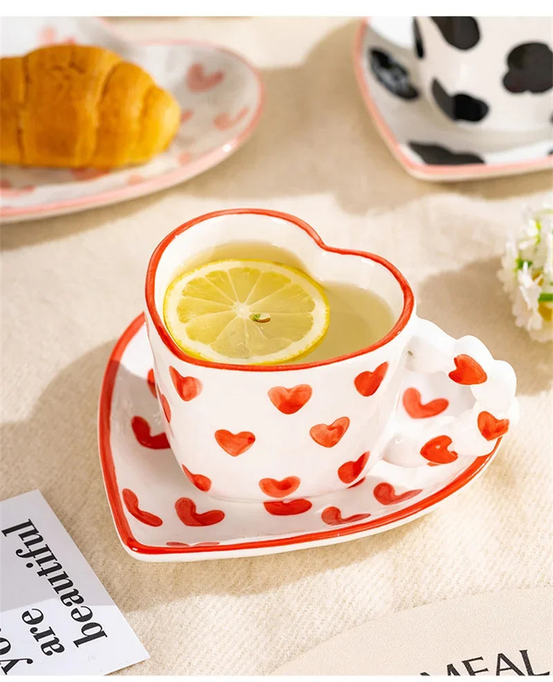 Heart-shaped mug with red heart patterns containing lemon slices and tea, placed on a beige surface.