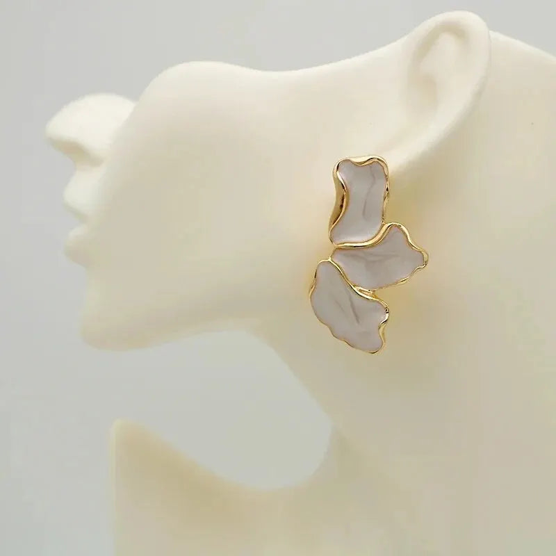 Gold and white earrings on a mannequin ear