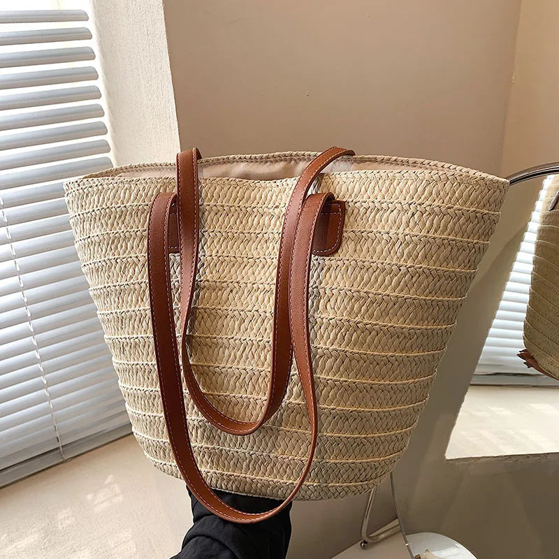 Woven straw tote bag with brown leather handles on a neutral background