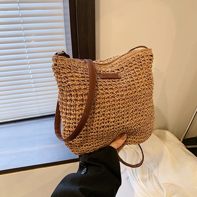 Woven handbag with brown leather straps held by a person indoors.