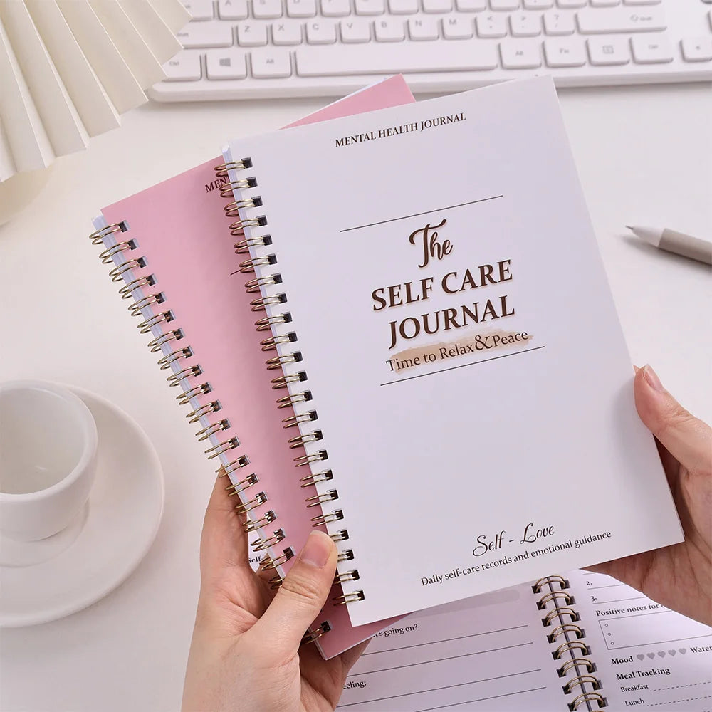 Person holding a self-care journal with a keyboard and cup in the background