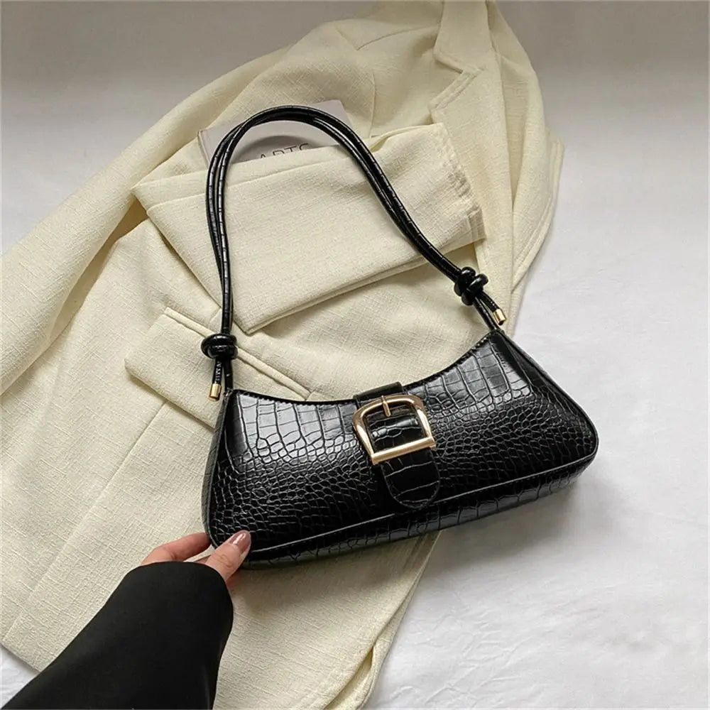 Black crocodile-patterned handbag with gold buckle held by a hand on a light background