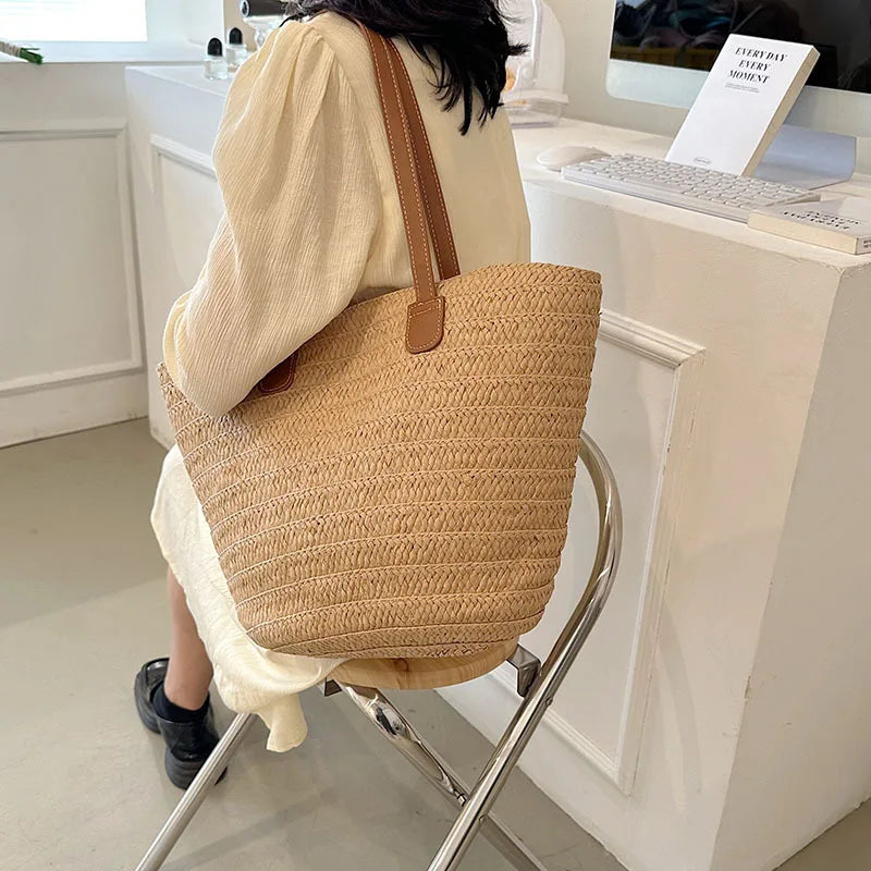Person sitting with a large woven beige bag over their shoulder in an indoor setting.