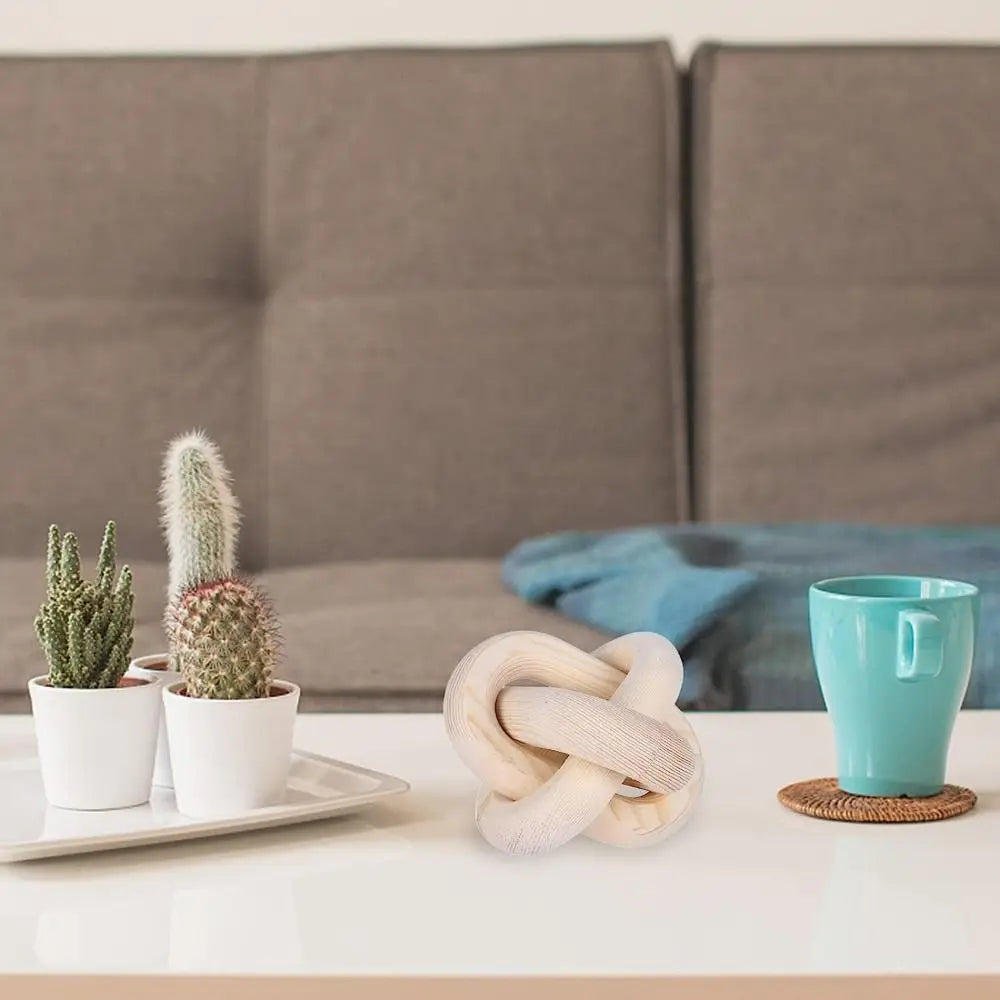 Decorative items including a knot sculpture, cacti, and a turquoise mug on a table with a gray sofa in the background.