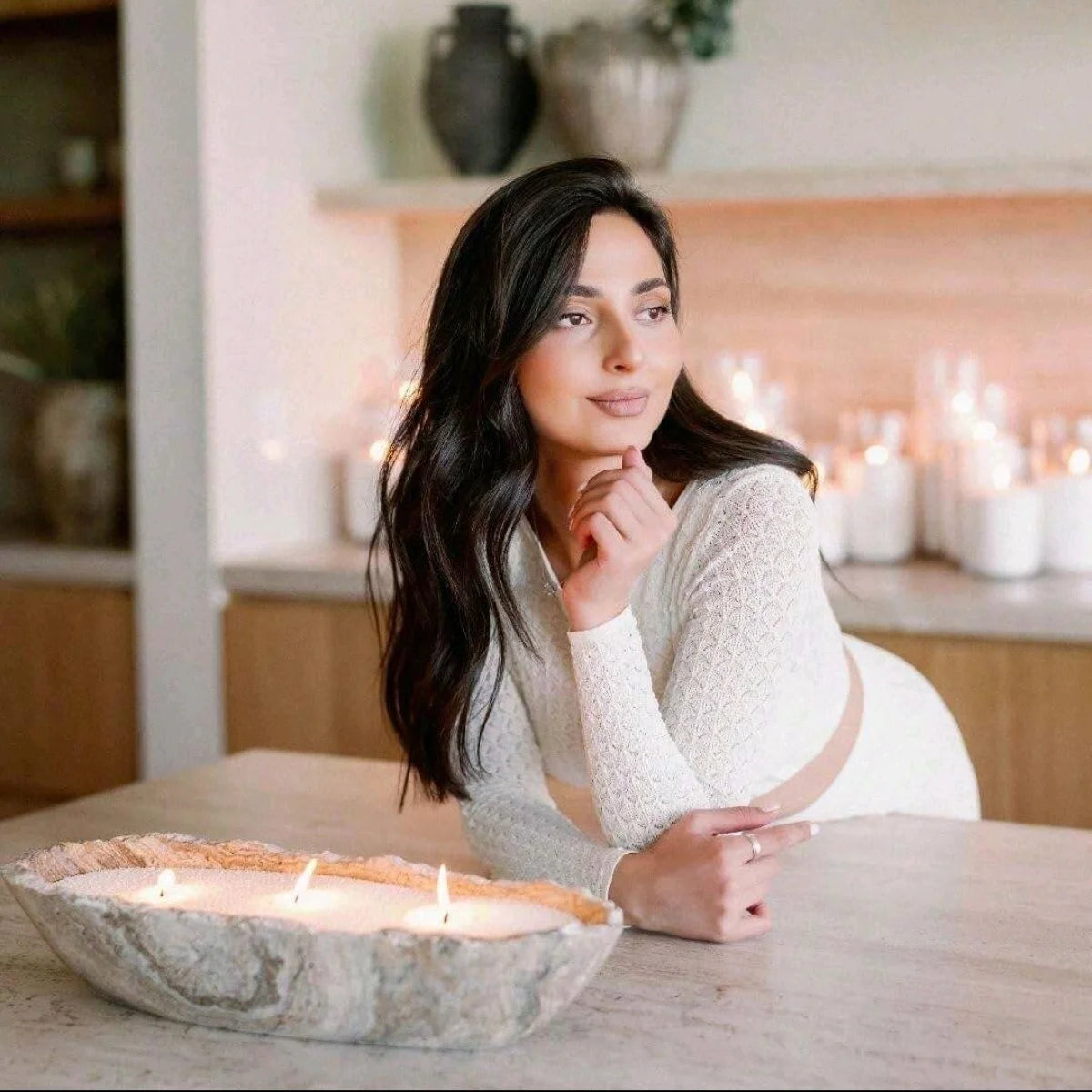 Woman sitting at a table with a bowl of candles in a softly lit room.
