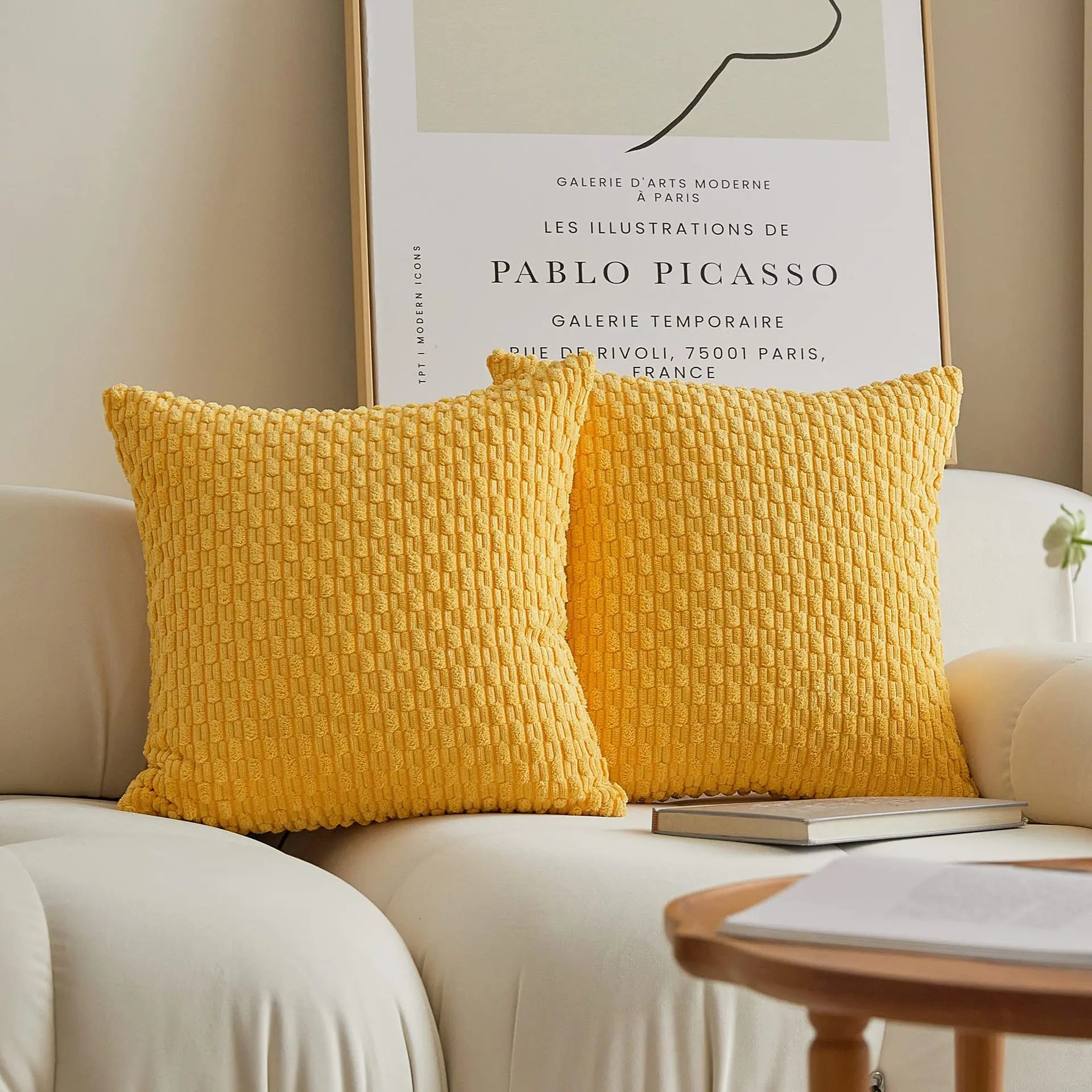 Yellow textured pillows on a beige sofa with a Picasso poster in the background