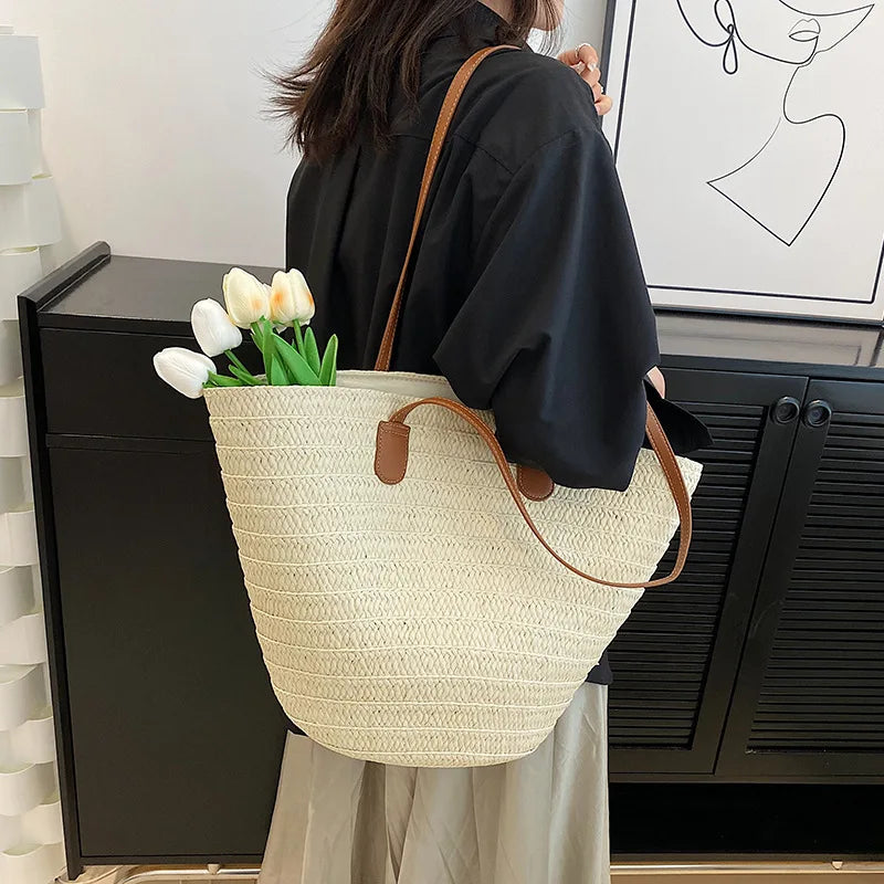 Person holding a straw tote bag with flowers indoors.